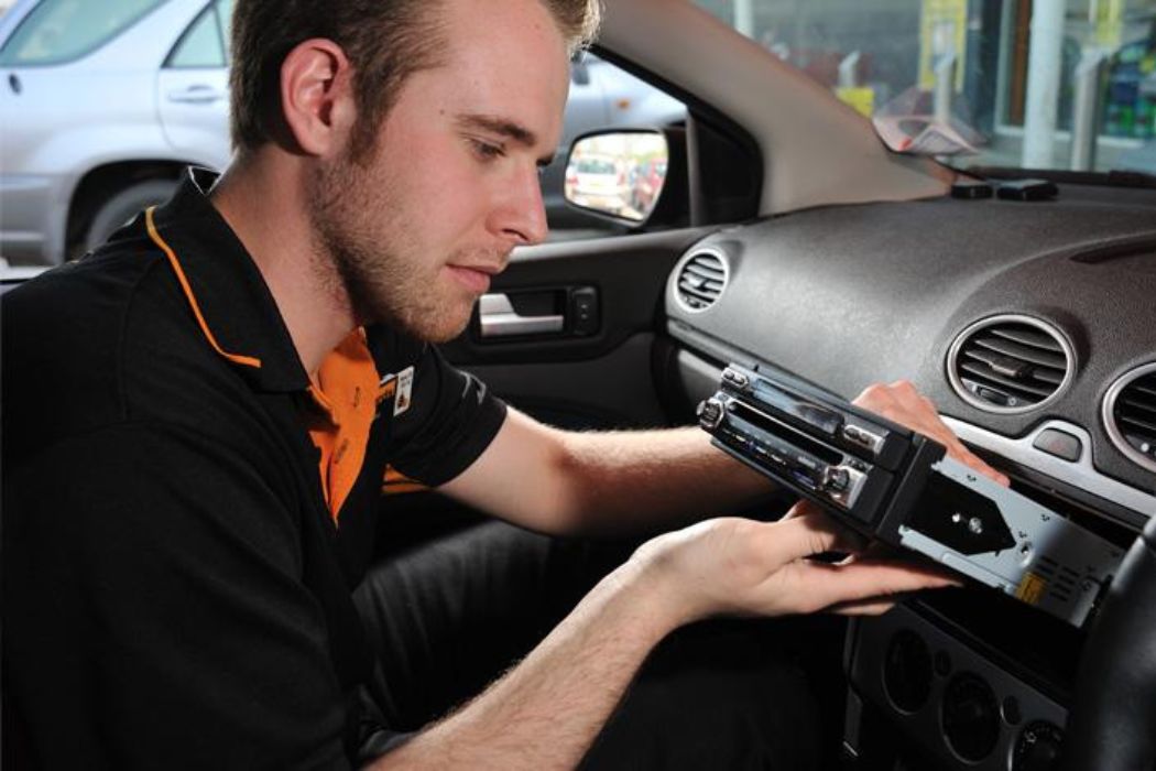 A man is intently repairing a car stereo inside a vehicle