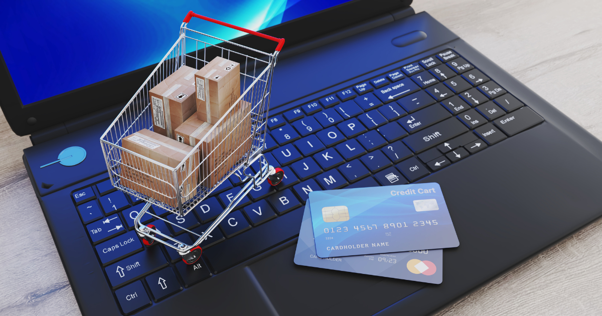 Online shopping concept with a miniature cart full of packages on a laptop keyboard and credit cards, symbolizing e-commerce transactions and digital payments.